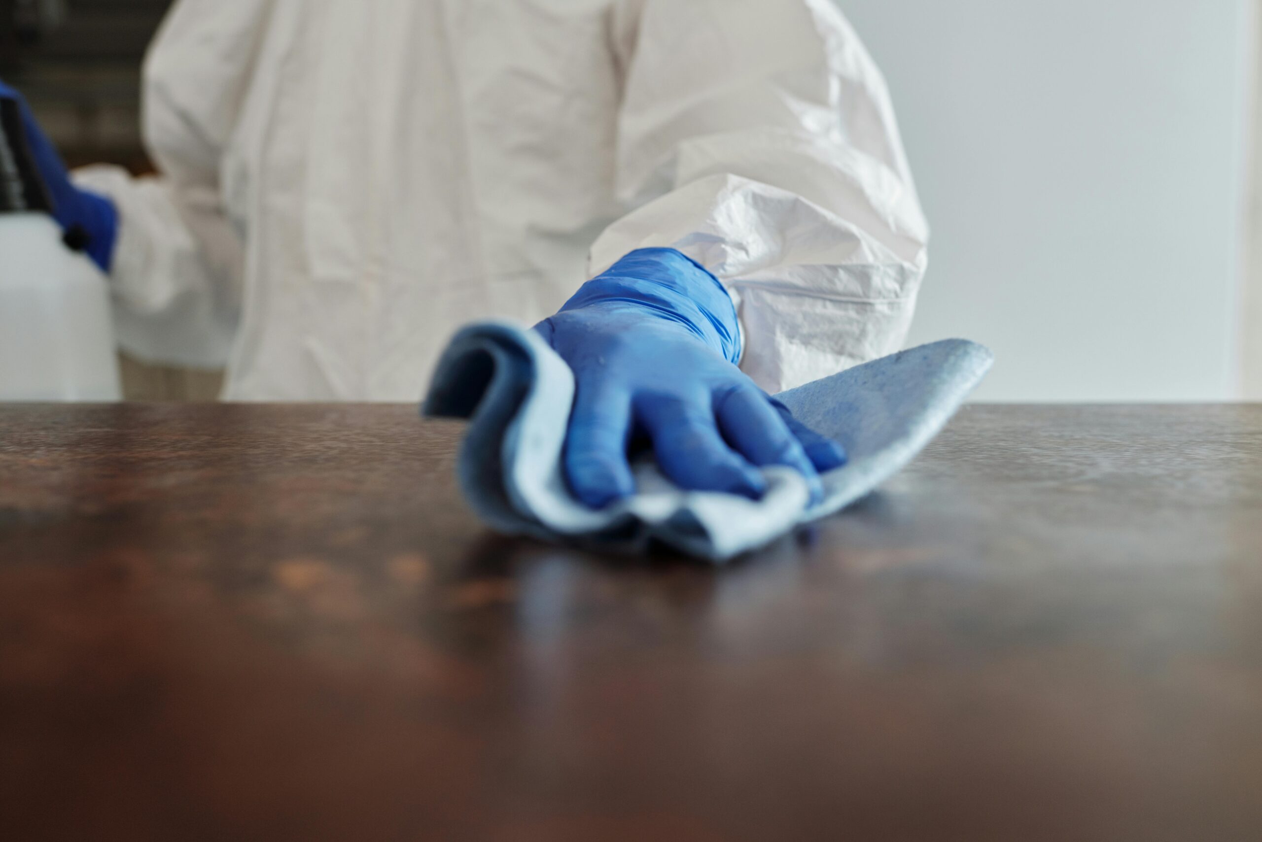 hand in blue rubber glove cleaning a wood table house cleaners in worcester